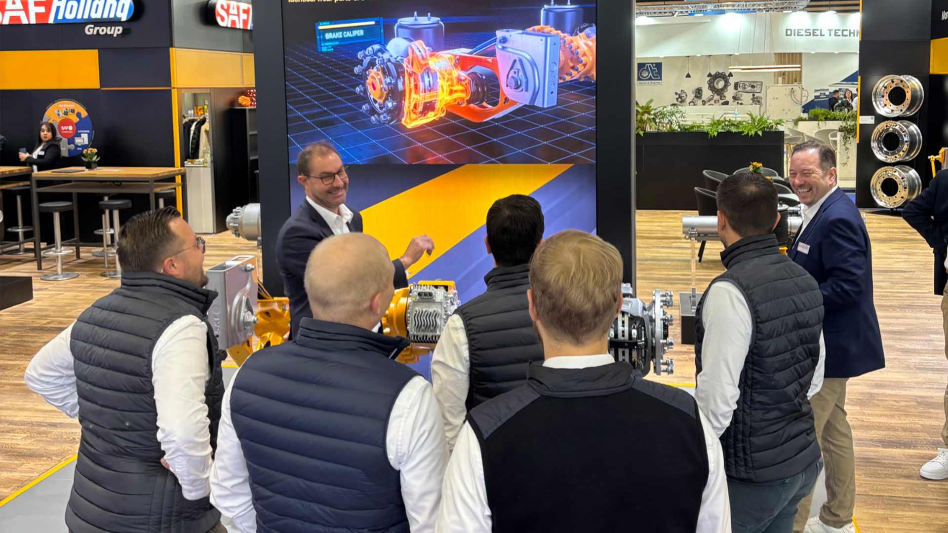 SAF-HOLLAND exhibition booth showing axle systems, with a presenter engaging with attendees.